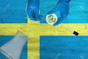 Sweden flag on laboratory table. Medical healthcare technologist holding COVID-19 swab collection kit, wearing blue protective gloves, epidemic concept.